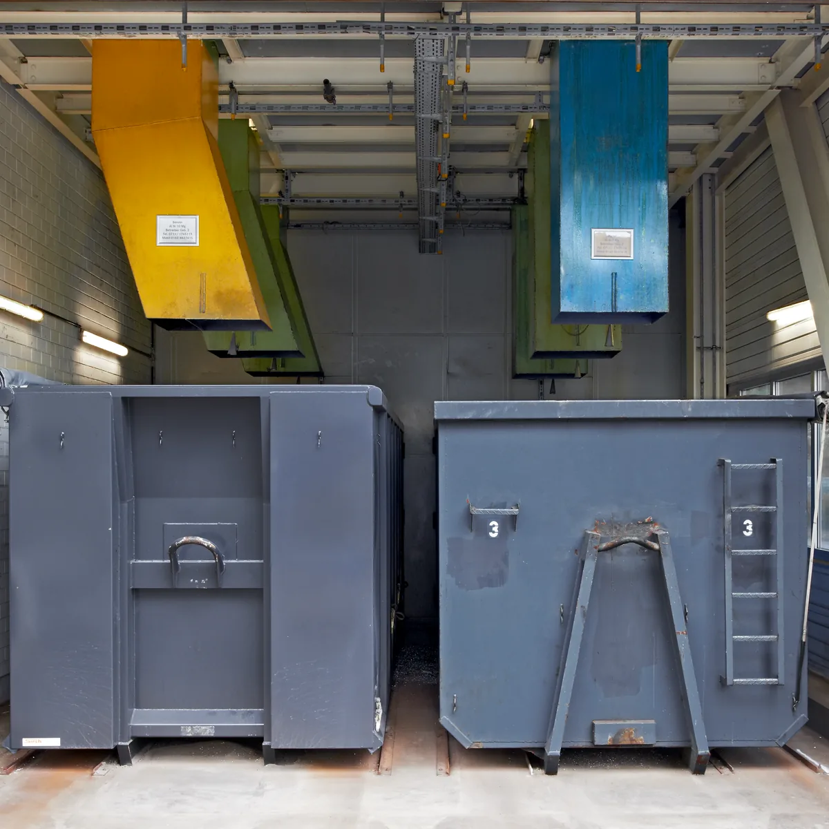 Containerbeschickung: farbige Abwurfrutschen über Sammelcontainern